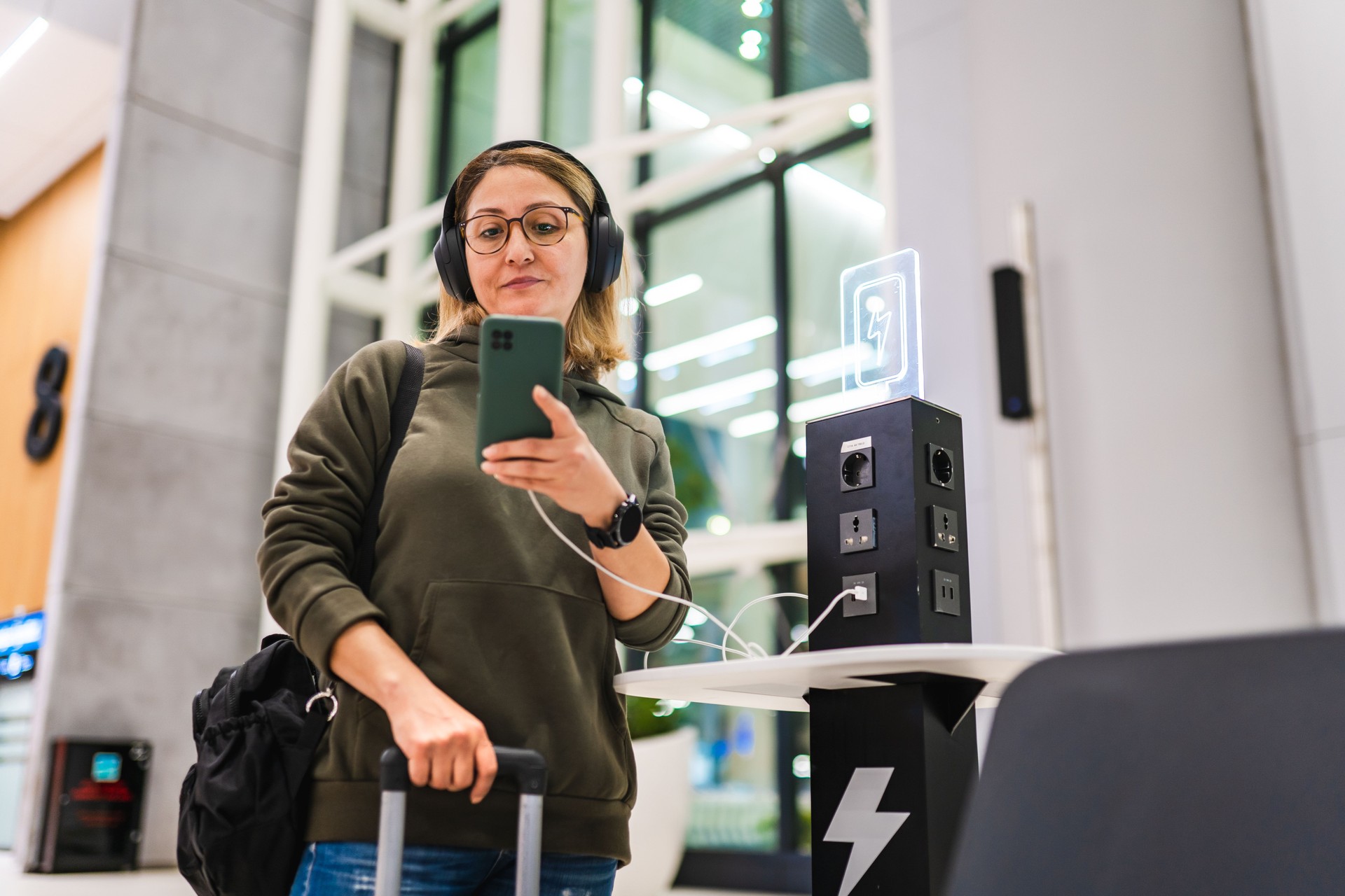 Woman waiting for her flight at the airport while charging her phone at charging station